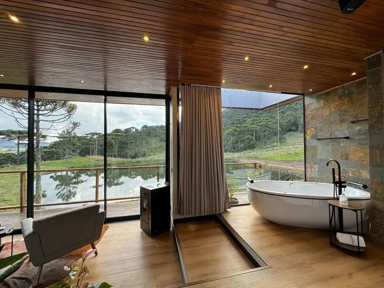 Banheira de imersão diante da janela com vista para o lago e as araucárias