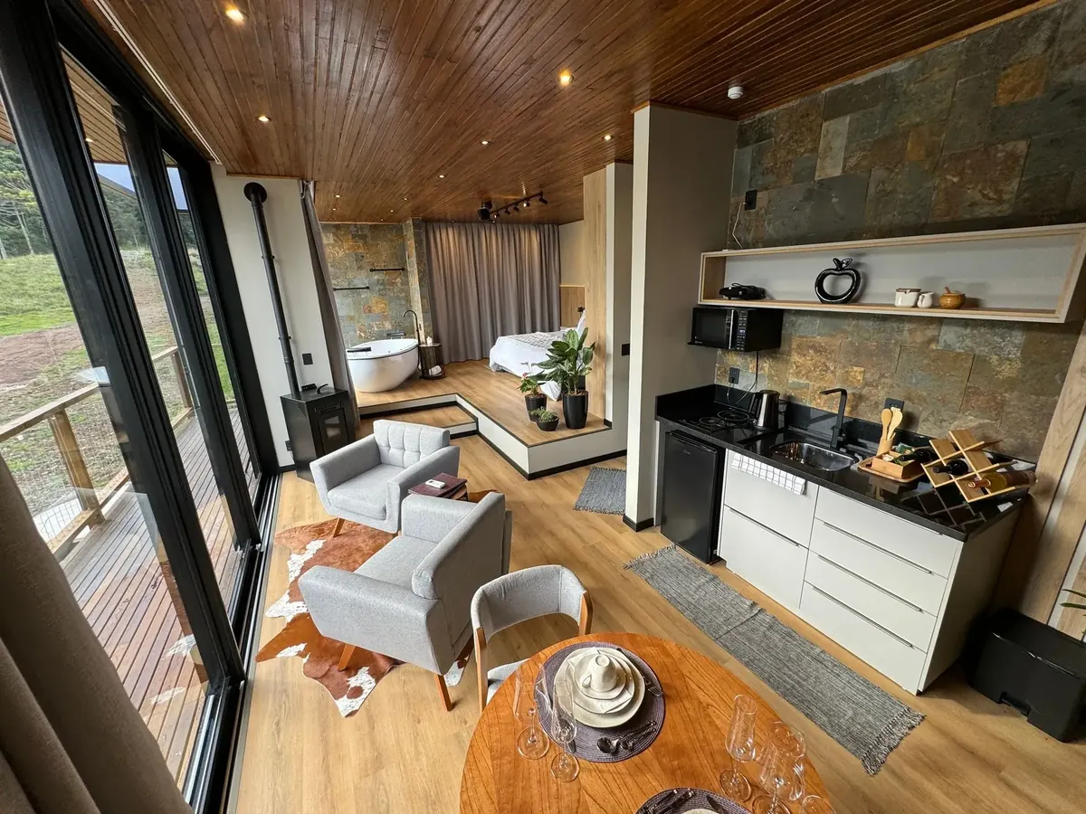 Sala de estar da cabana com poltronas e parede de vidro