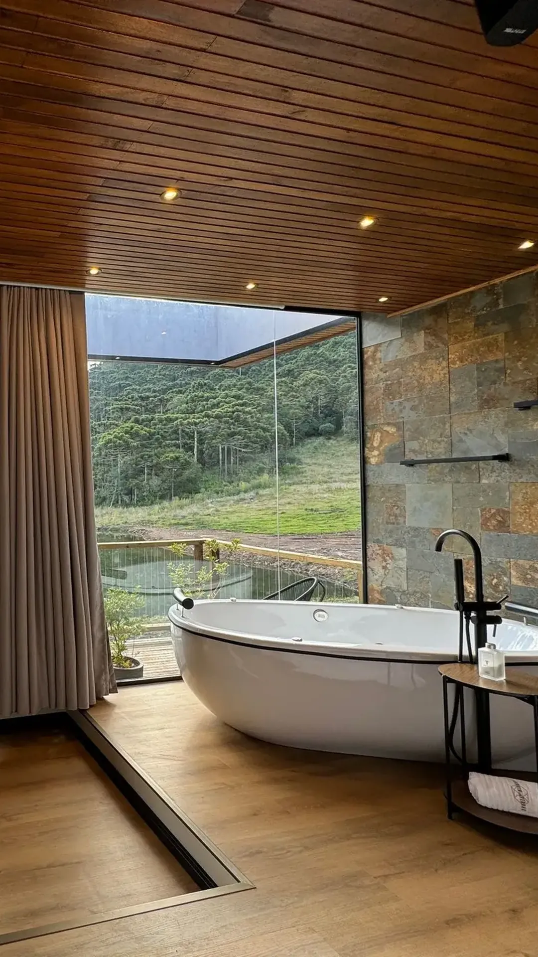 Banheira de imersão diante da parede de vidro, com vista para o lago